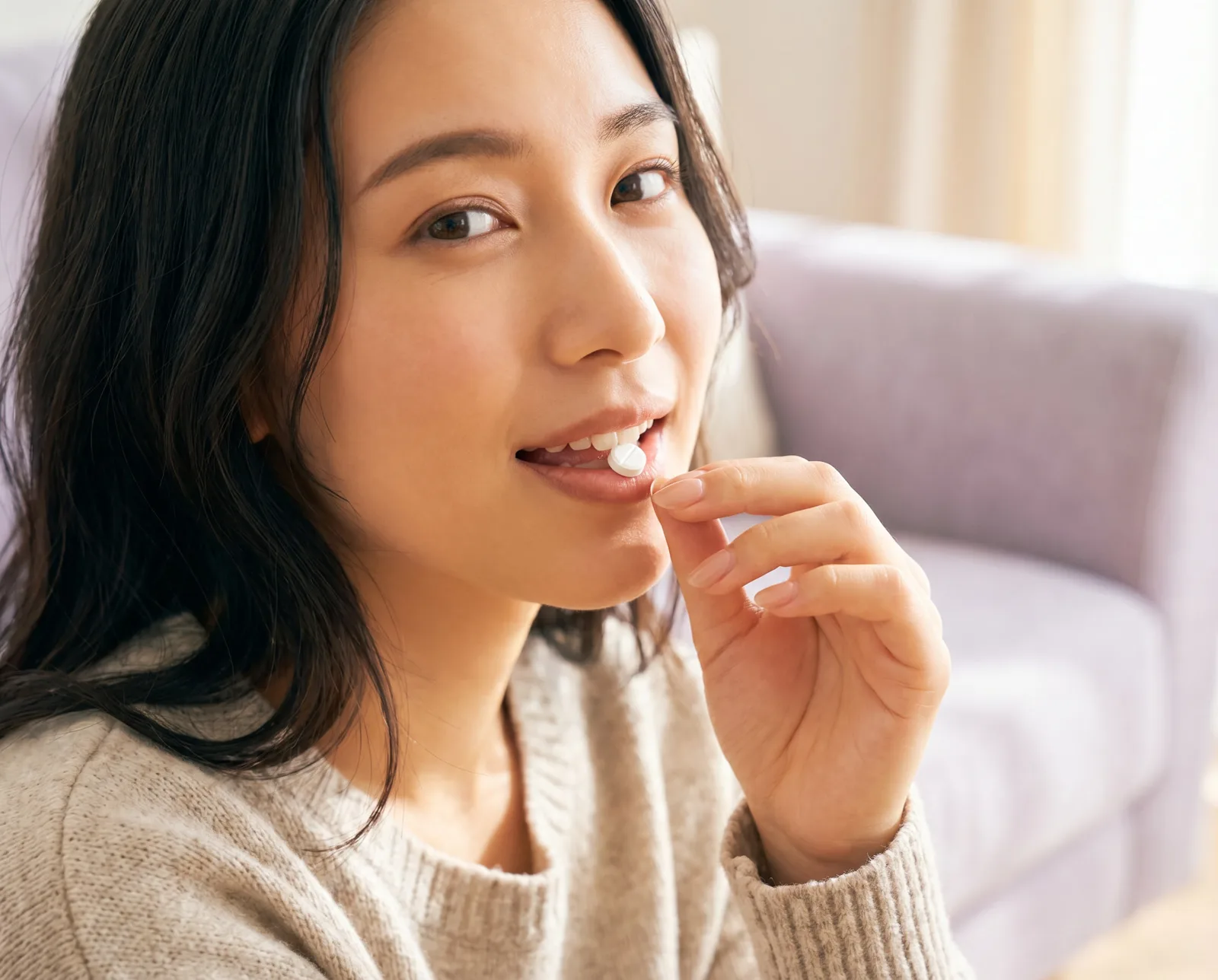 自宅のソファで錠剤を口に運ぶ女性